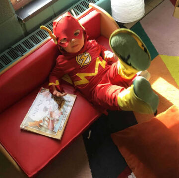 A young boy sits on a bench while dressed up as the Flash for Halloween.