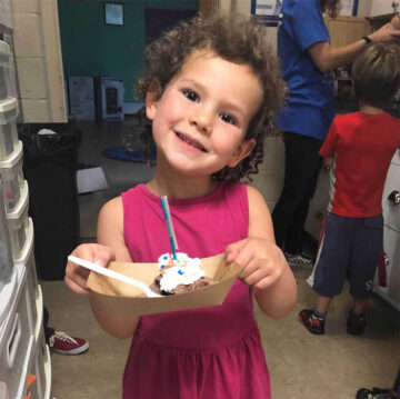 A young girl smiles while holding ice cream with a birthday candle.