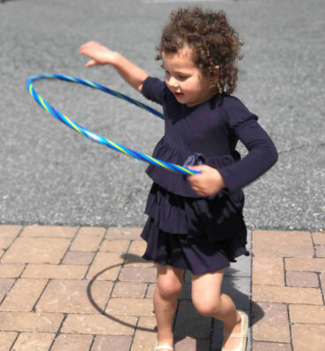 A young girl in a blue dress hula hoops.