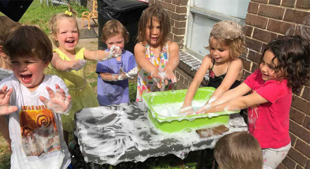 Children play with soapy water on a small table outside.